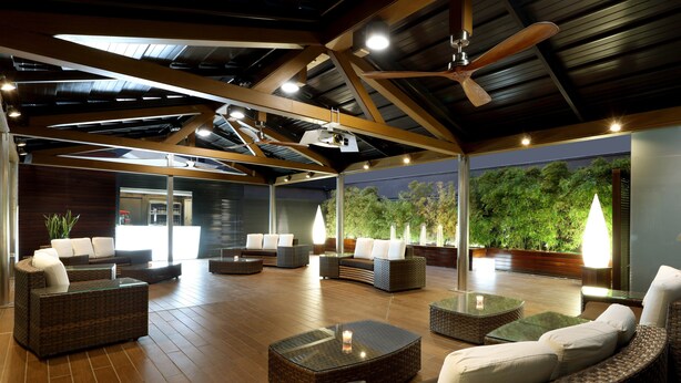 An outdoor lounge area with wicker furniture, a ceiling fan, and a view of greenery.