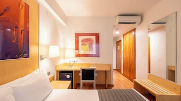 Habitación de hotel con cama, escritorio, silla y un espejo grande.