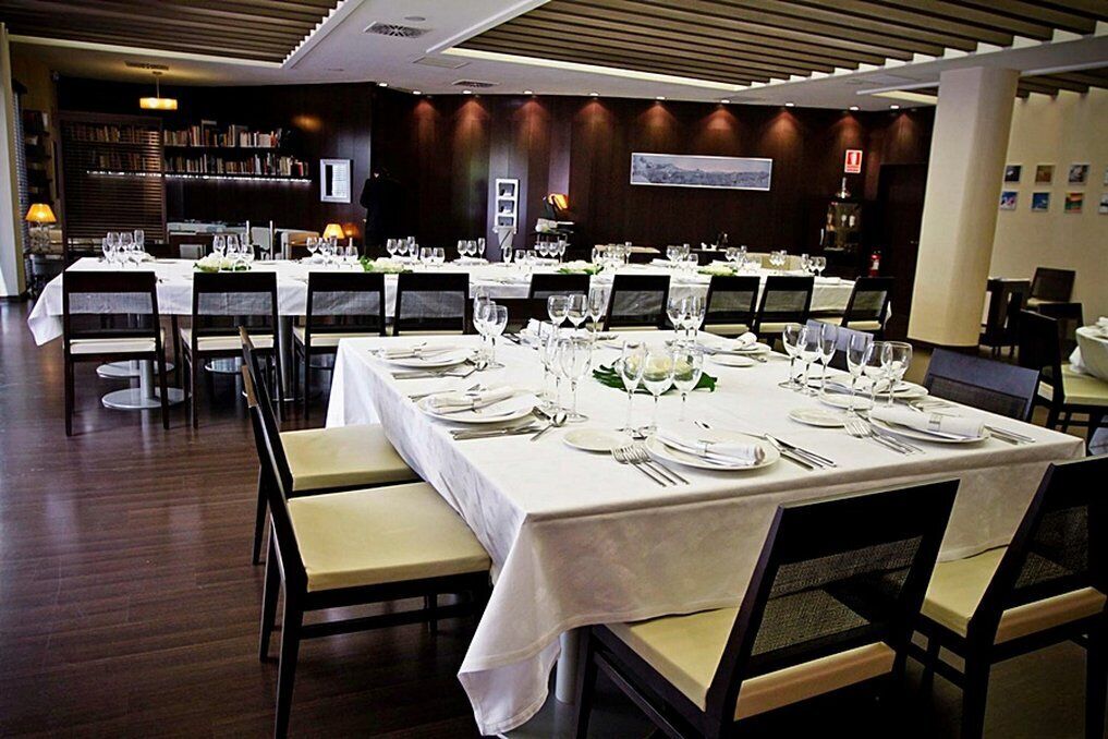 Een stijlvol restaurantgedeelte met meerdere gedekte tafels, met witte tafelkleden en netjes opgemaakte servies.