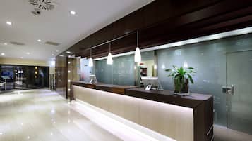 A modern hotel reception area with a wooden reception desk, pendant lighting, and a glass wall displaying the hotel's name.