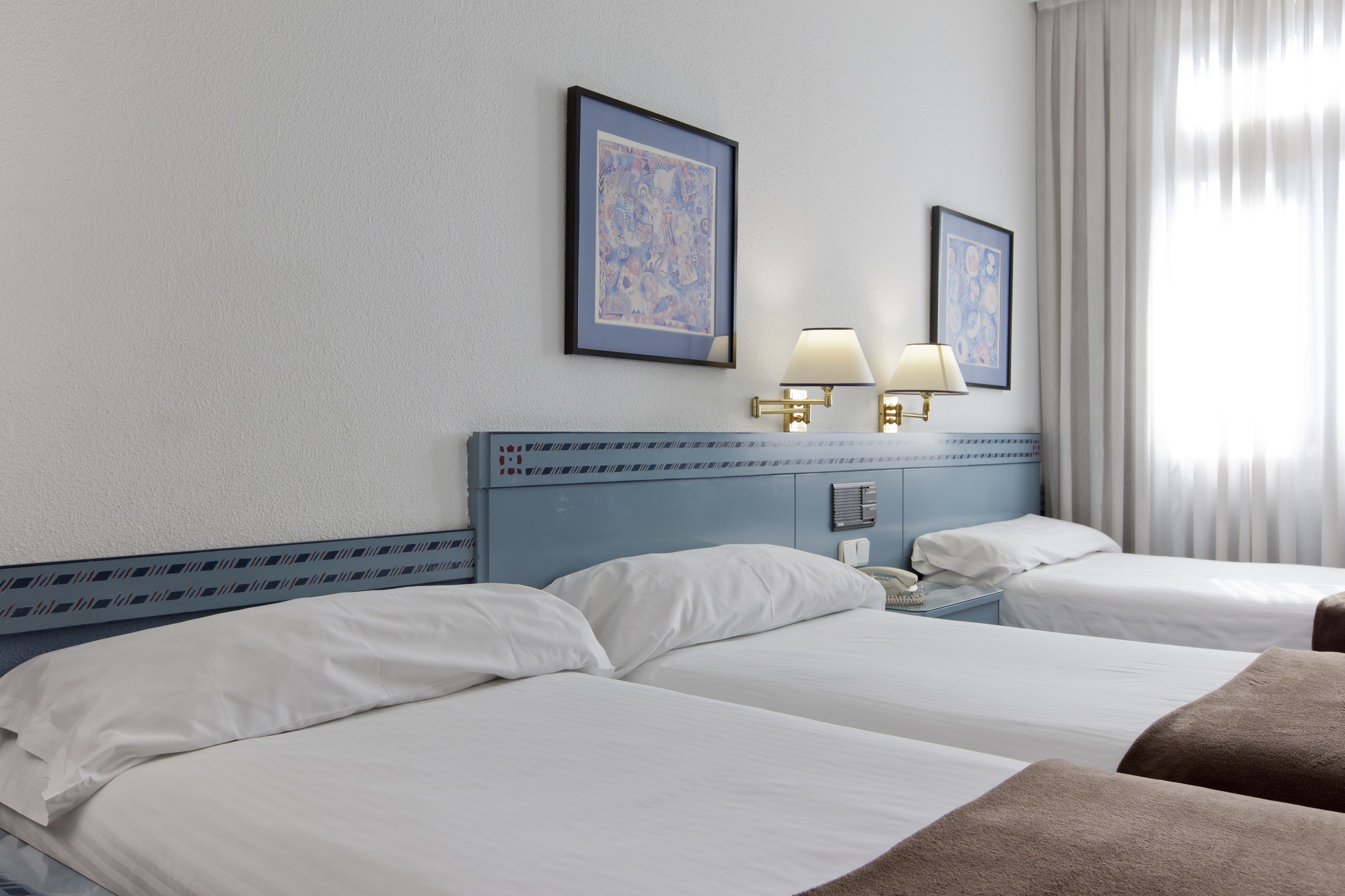 Ein Hotelzimmer mit zwei Betten, einem Versteck mit dekorativem Muster, zwei Wandlampen und zwei gerahmten Bildern an der Wand.