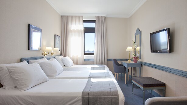 A hotel room with two beds, a desk, a chair, a TV, and a window with curtains. - Espahotel Gran Via (Madrid)