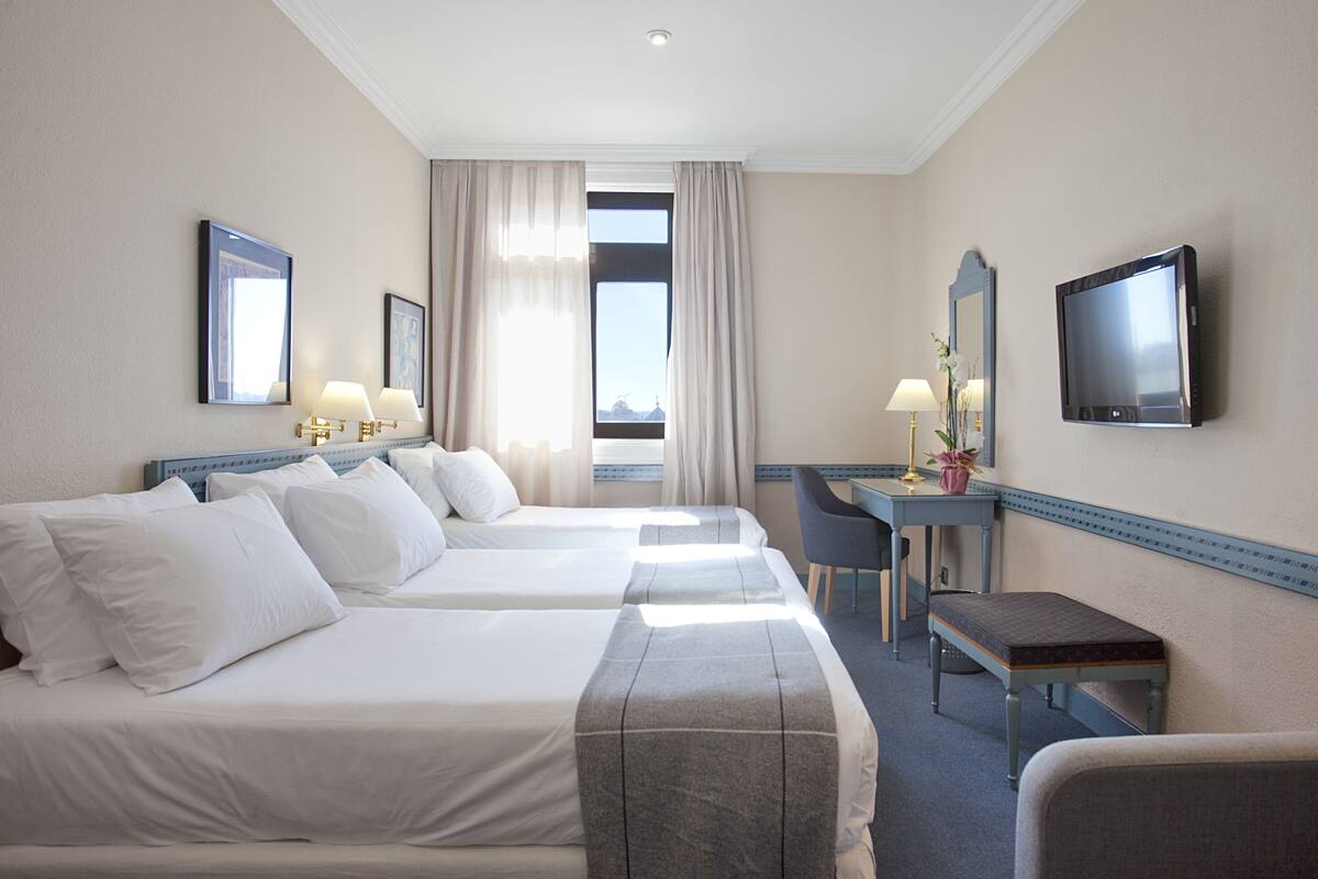 A hotel room with two beds, a desk, a chair, a TV, and a window with curtains.