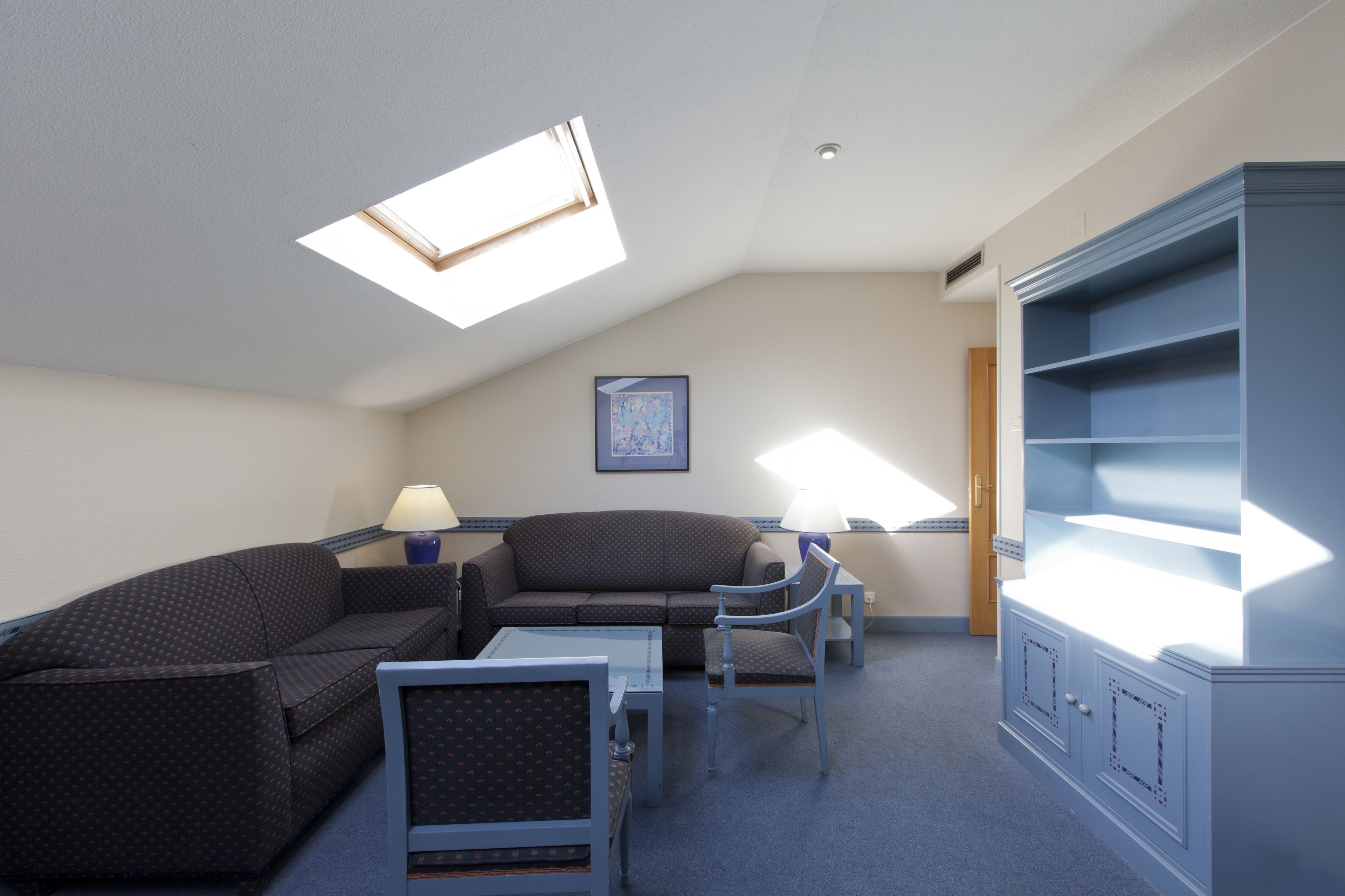 A room with a high ceiling, a skylight, a sofa, a chair, a small table, and a cabinet.