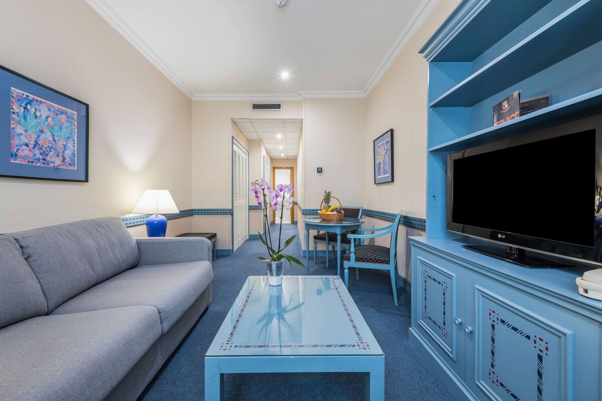 A living room with a sofa, a coffee table, a TV, and a dining area with chairs and a table.