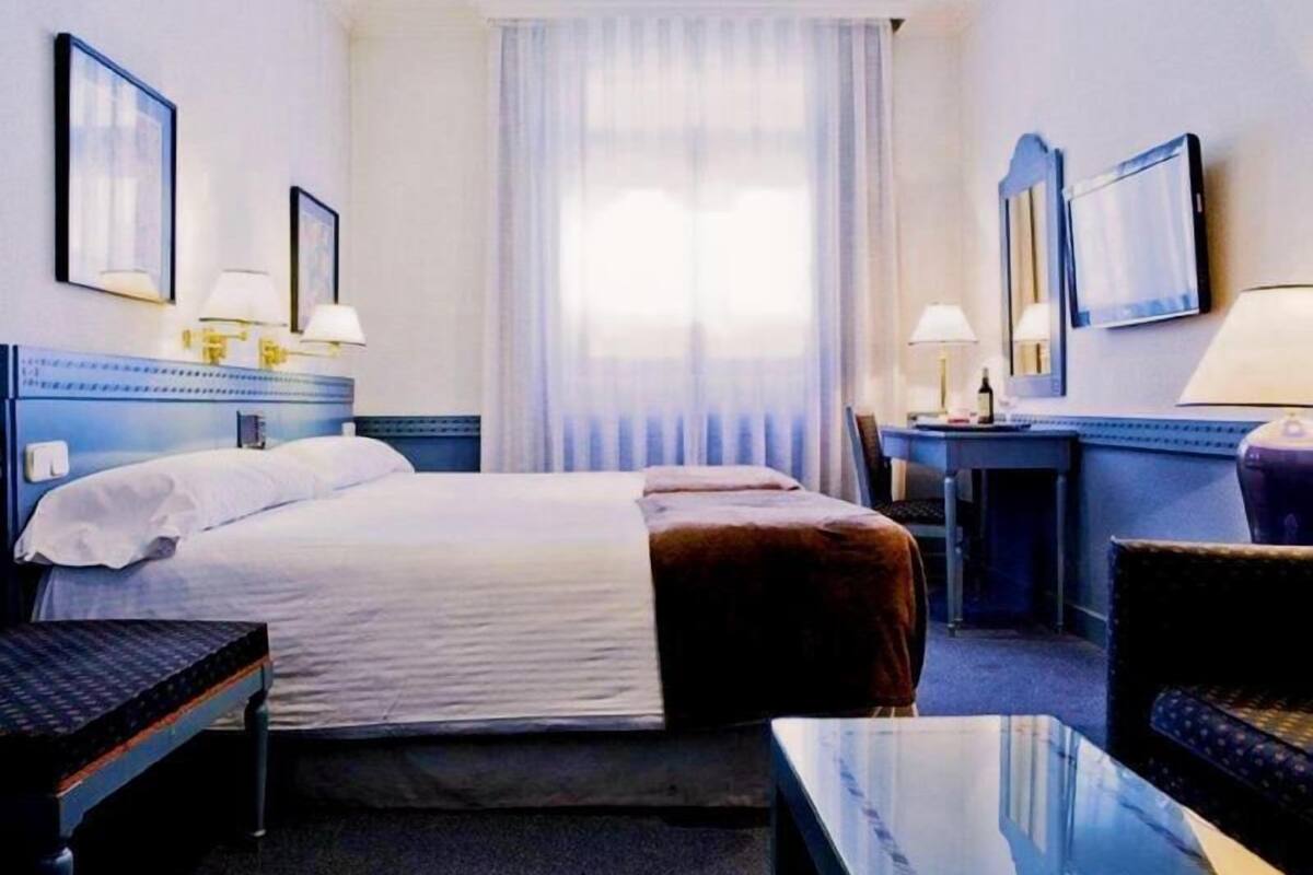 A hotel room with a bed, bedside tables, a desk, and a chair.