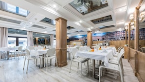 A restaurant with white tables and chairs, wooden pillars, and a large bookshelf in the background. - Espahotel Gran Via (Madrid)