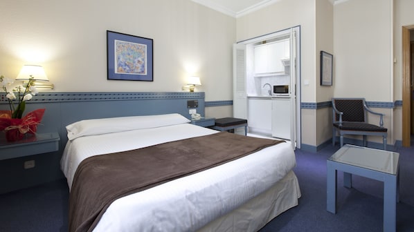 A hotel room with a bed, bedside table, lamp, framed artwork, and a chair.