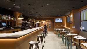 A bar area with a long counter, stools, and a television screen. - Hotel Yoldi (Pamplona)