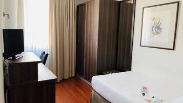 Una habitación de hotel con cama, escritorio, televisor y armario.