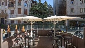 An outdoor cafe with tables and chairs, umbrellas, and a view of a historic building in the background. - Hotel Yoldi (Pamplona)