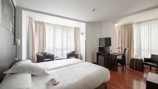 A hotel room with two beds, a desk with a TV, and two chairs. - Hotel Yoldi (Pamplona)