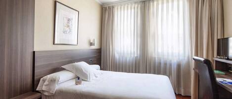 A hotel room with a large bed, a desk with a chair, a television, and a window with curtains.