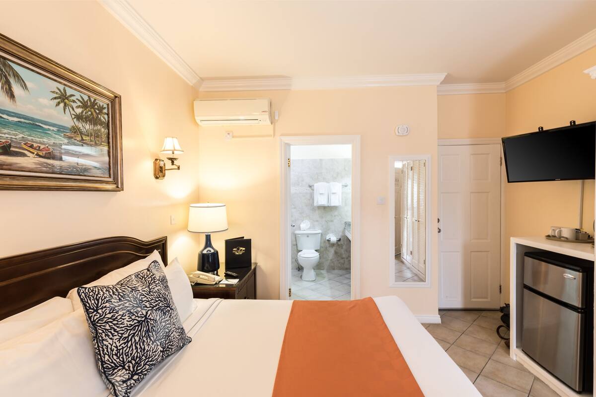 A hotel room with a bed, a nightstand, a TV, and a view of the bathroom.