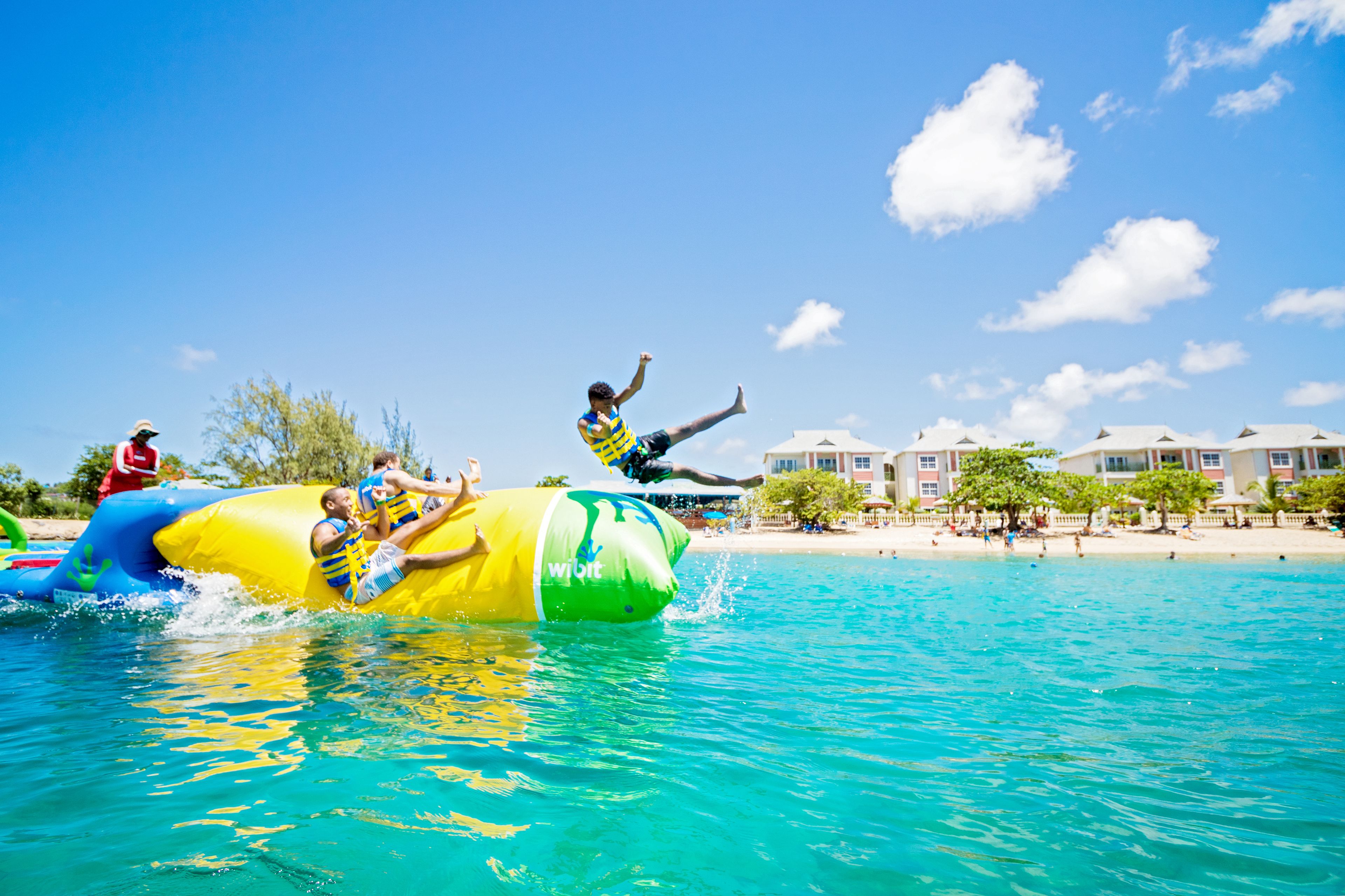 A water park with inflatable water slides and a beach area with buildings in the background.