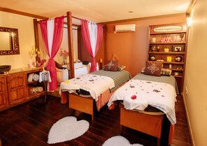 A room with two wooden beds, a vanity with a mirror, a shelf with herbal supplements, and a heart-shaped rug.