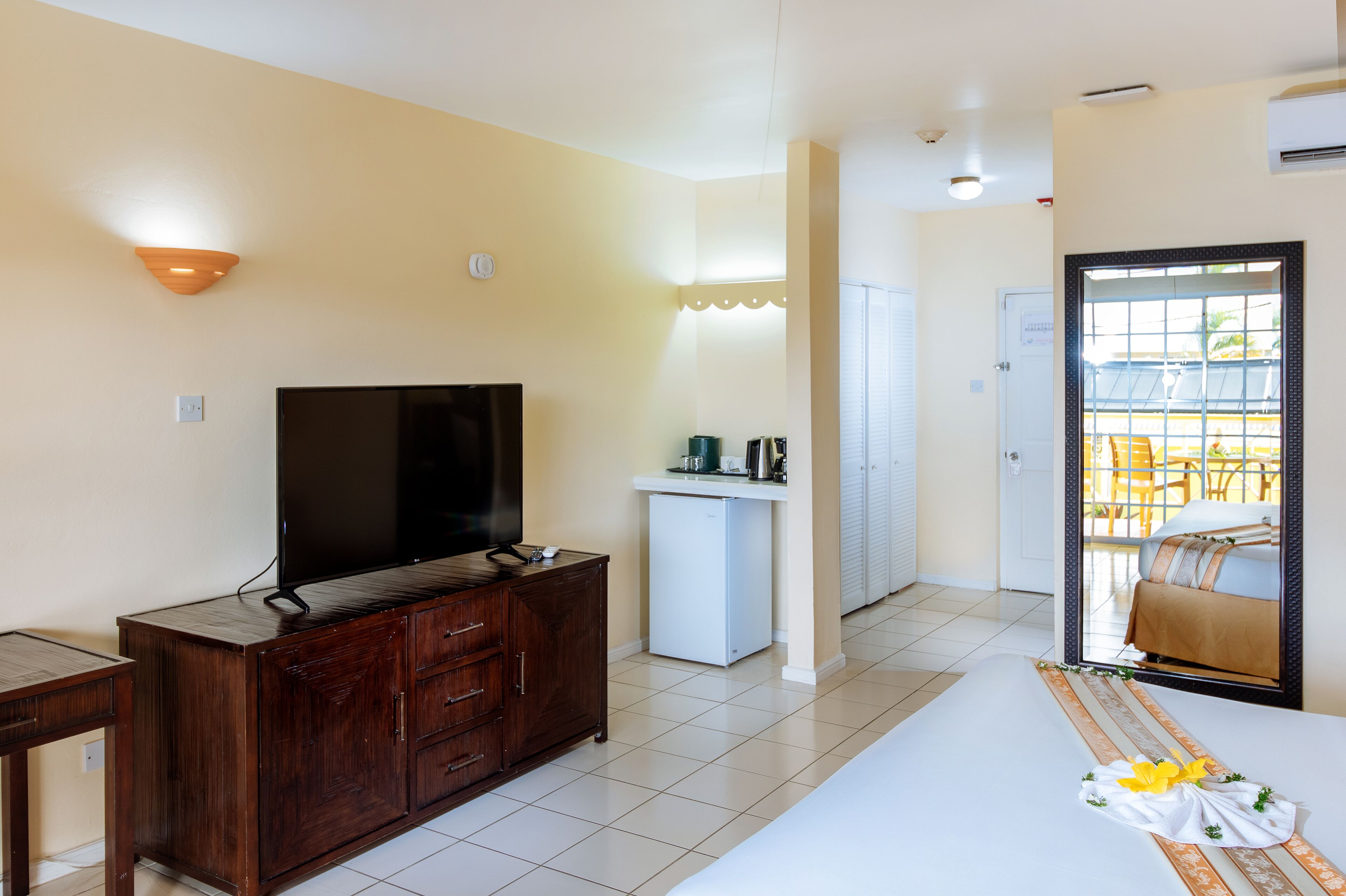 A hotel room with a TV, wooden cabinet, small kitchenette, and a bed with a decorative pillow.