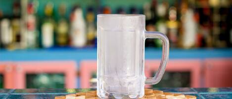 A clear glass mug on a wooden coaster at a bar with a blurred background of bottles.