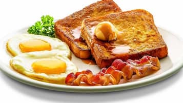 Un plato con dos huevos fritos, dos rebanadas de tostada con mantequilla y tocino.