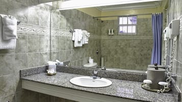 Un baño con lavamanos de encimera de granito, un espejo, toallero, cortina de ducha y secador de pelo.