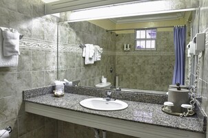 Un baño con lavamanos de encimera de granito, un espejo, toallero, cortina de ducha y secador de pelo.
