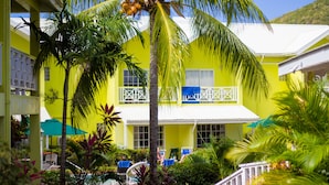 A bright yellow building with a white balcony, surrounded by palm trees and a pool area. - Bay Gardens Hotel (Gros Islet)
