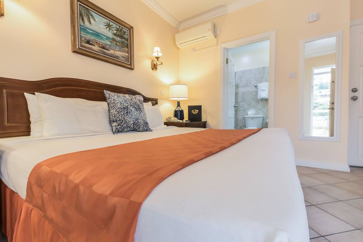 A hotel room with a large bed, a nightstand with a lamp, a framed picture on the wall, and a bathroom door.