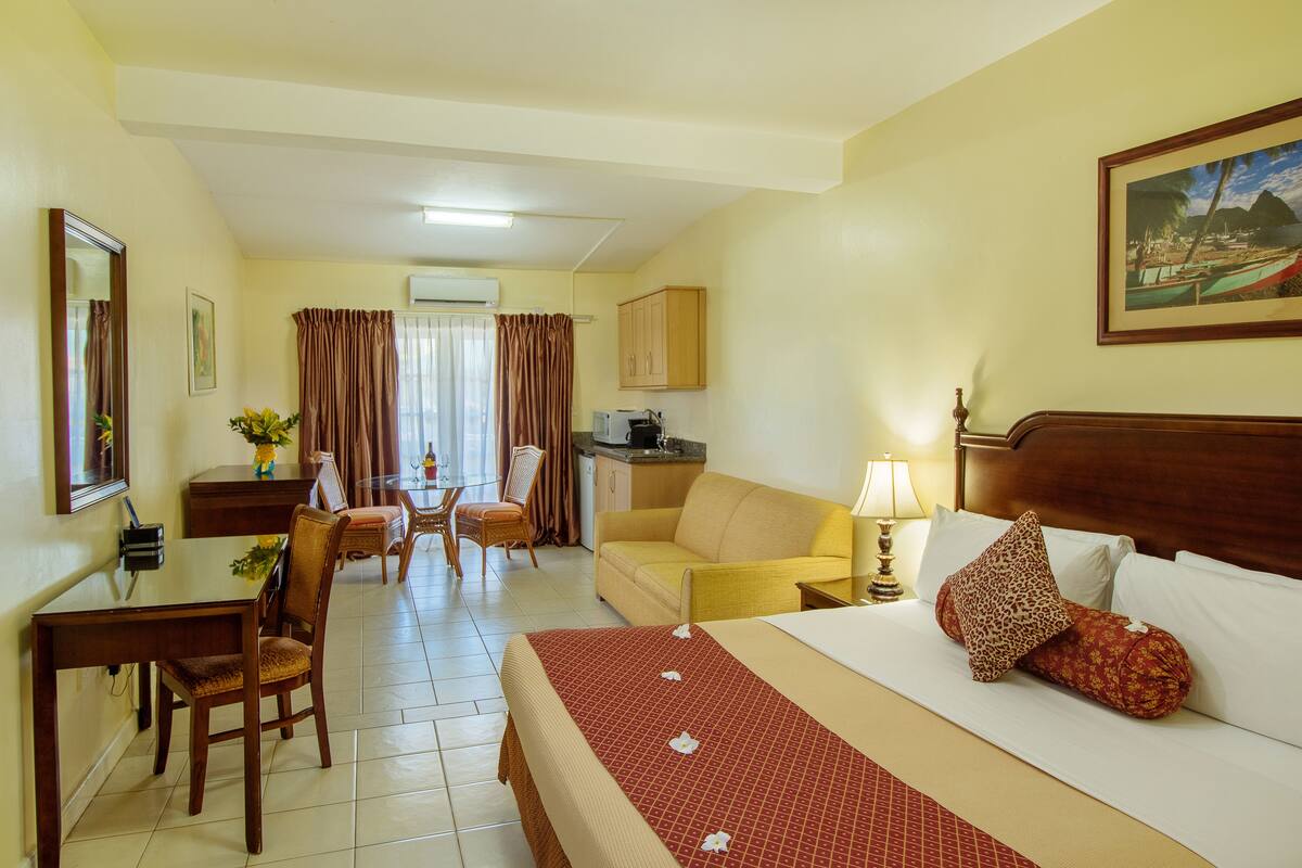 A hotel room with a bed, a desk, a chair, a sofa, a dining table, and a kitchen area.