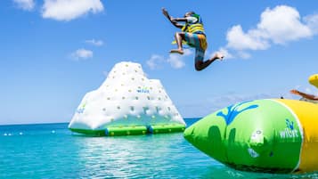 Una persona salta d'una estructura inflable verda i groga a l'aigua, amb una illa inflable blanca amb el lema "Wibit" al fons.