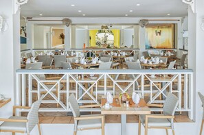 A restaurant with multiple tables and chairs, a central bar area, and a view of the outdoors. - Bay Gardens Hotel (Gros Islet)