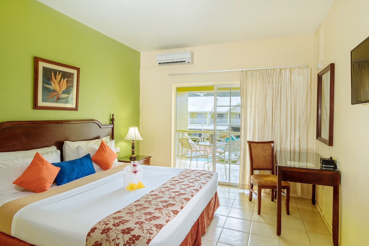 A hotel room with a bed, a desk, a chair, a balcony with a view, and an air conditioning unit.