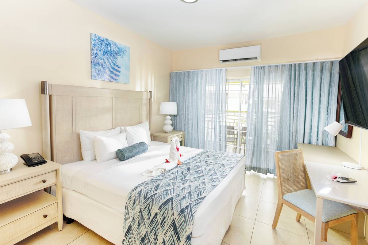 A hotel room with a bed, bedside tables, a desk, a chair, and a TV.