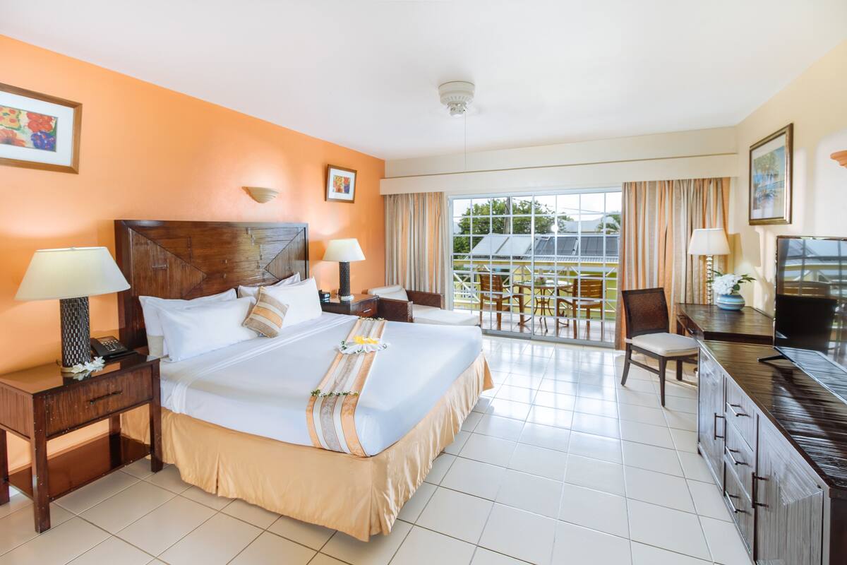 A hotel room with a bed, bedside tables, a desk, a chair, a television, and a balcony with a view.