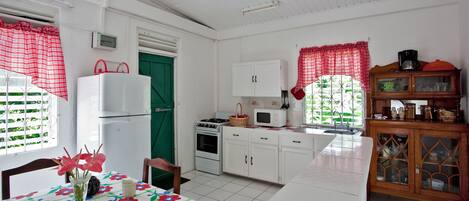 A kitchen with white cabinets, a refrigerator, a stove, and a microwave. There is a dining table with chairs and a vase of flowers.