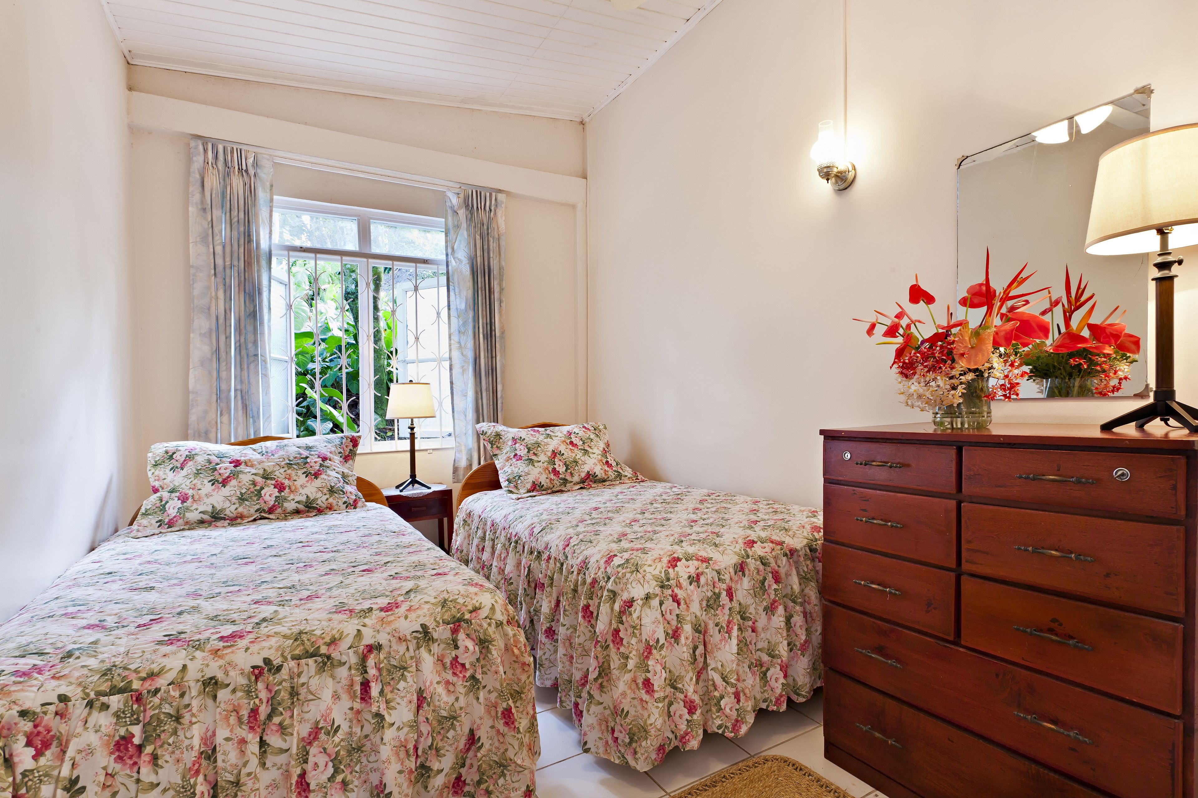 A bedroom with two beds, a dresser, a lamp, and a window with curtains.