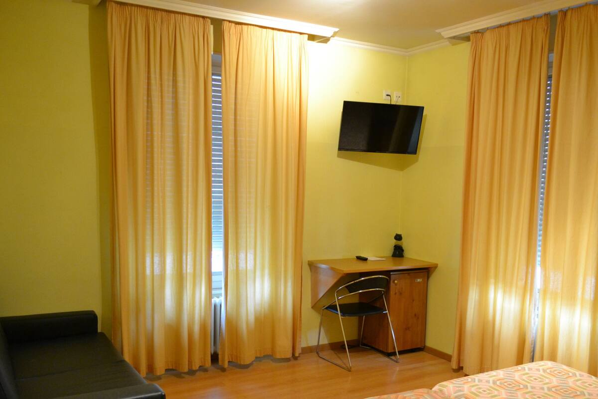 Una habitación de hotel con una cama, un escritorio, una silla y un televisor en la pared.