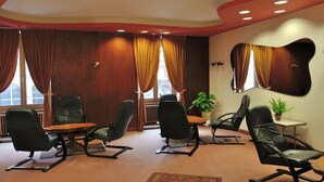 Un salón de conferencias con una mesa de madera, cuatro sillas negras y una planta en maceta.