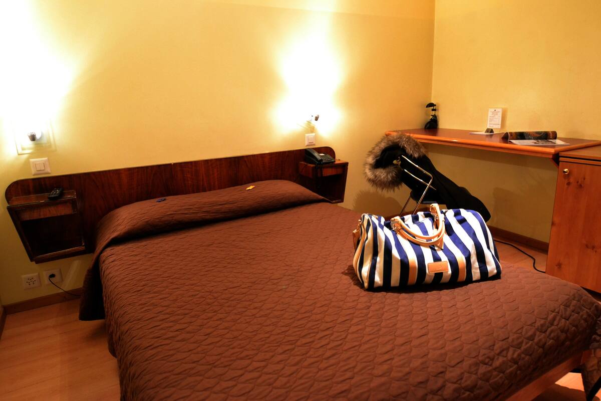 Una habitación de hotel con cama, mesita de noche, escritorio y lámpara.