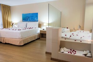 A hotel room with a double bed, a side table, a nightstand, a large mirror, a painting on the wall, and a bathtub with rose petals. - Holiday Inn Montevideo by IHG (Montevideo)