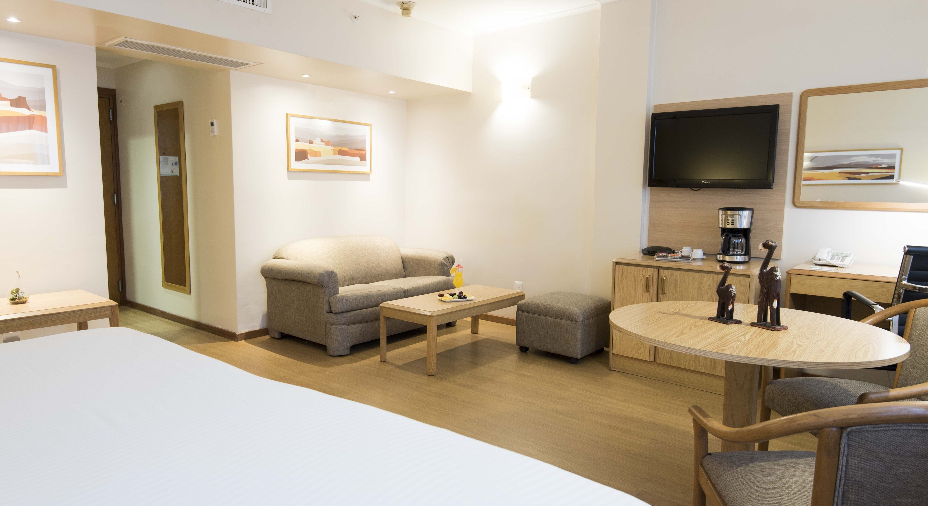 Una habitación de hotel con cama, sofá, mesa de centro, una mesa redonda de madera, televisor y un armario.