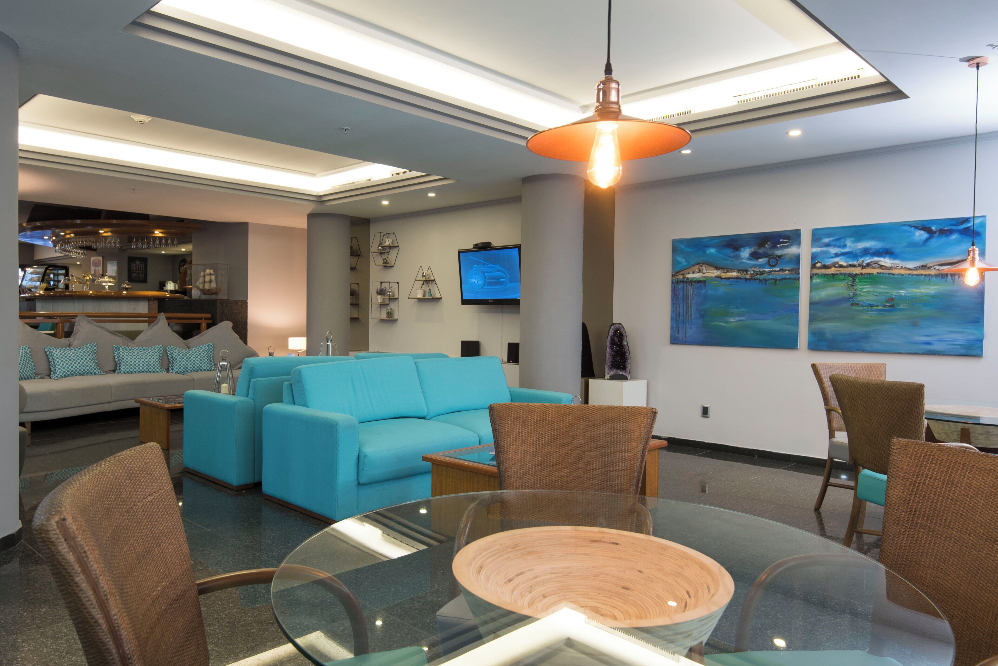 A modern living room with a blue sofa, glass dining table, and a bar area in the background.