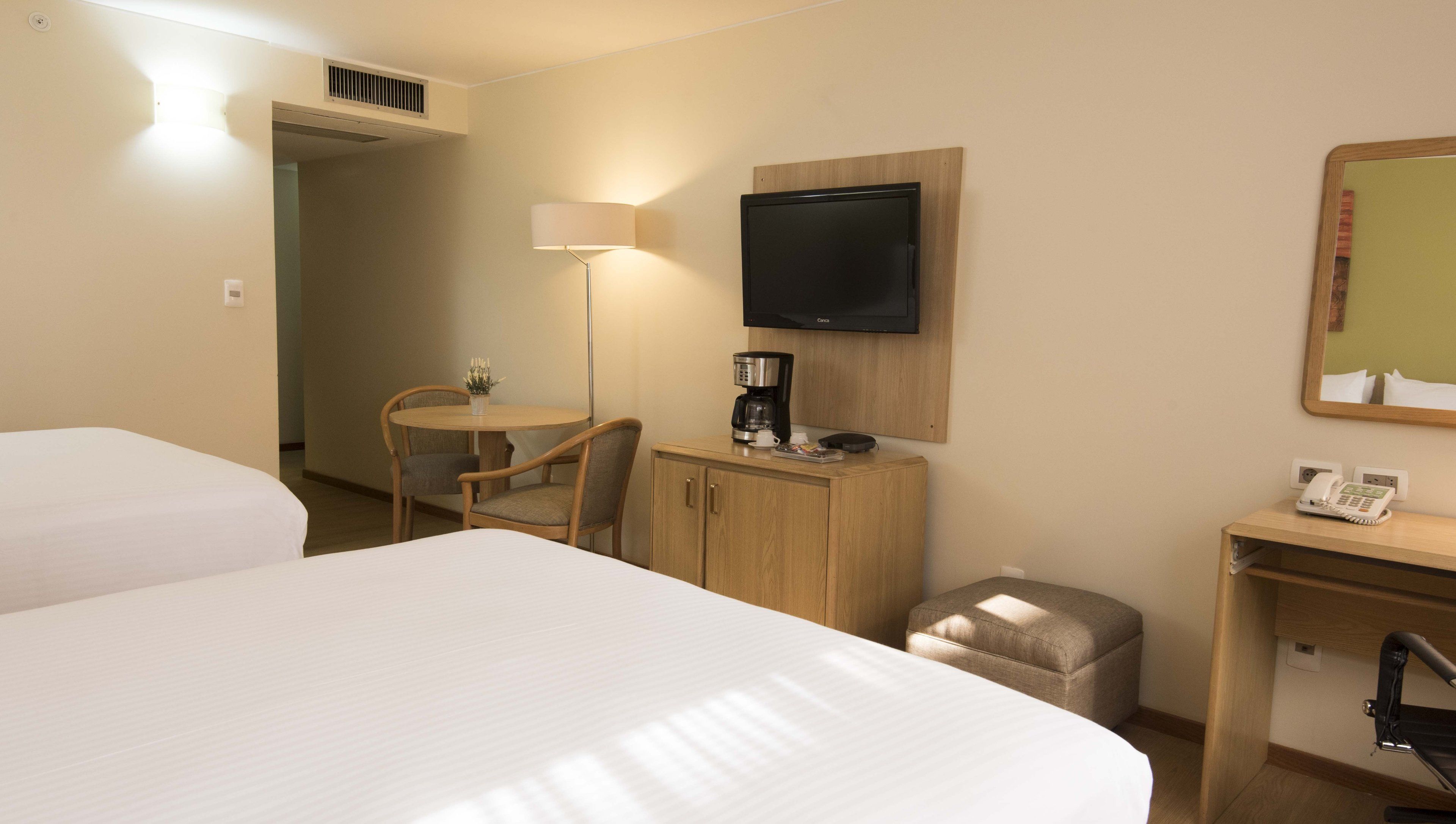 Habitación de hotel con dos camas, un escritorio con lámpara, televisión, un armario pequeño y teléfono.