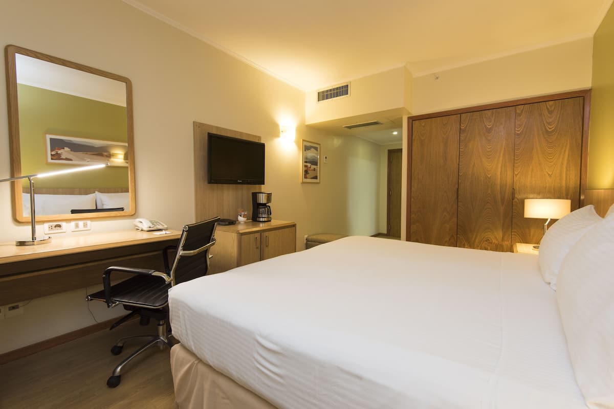 A hotel room with a bed, desk, chair, TV, and a wardrobe.