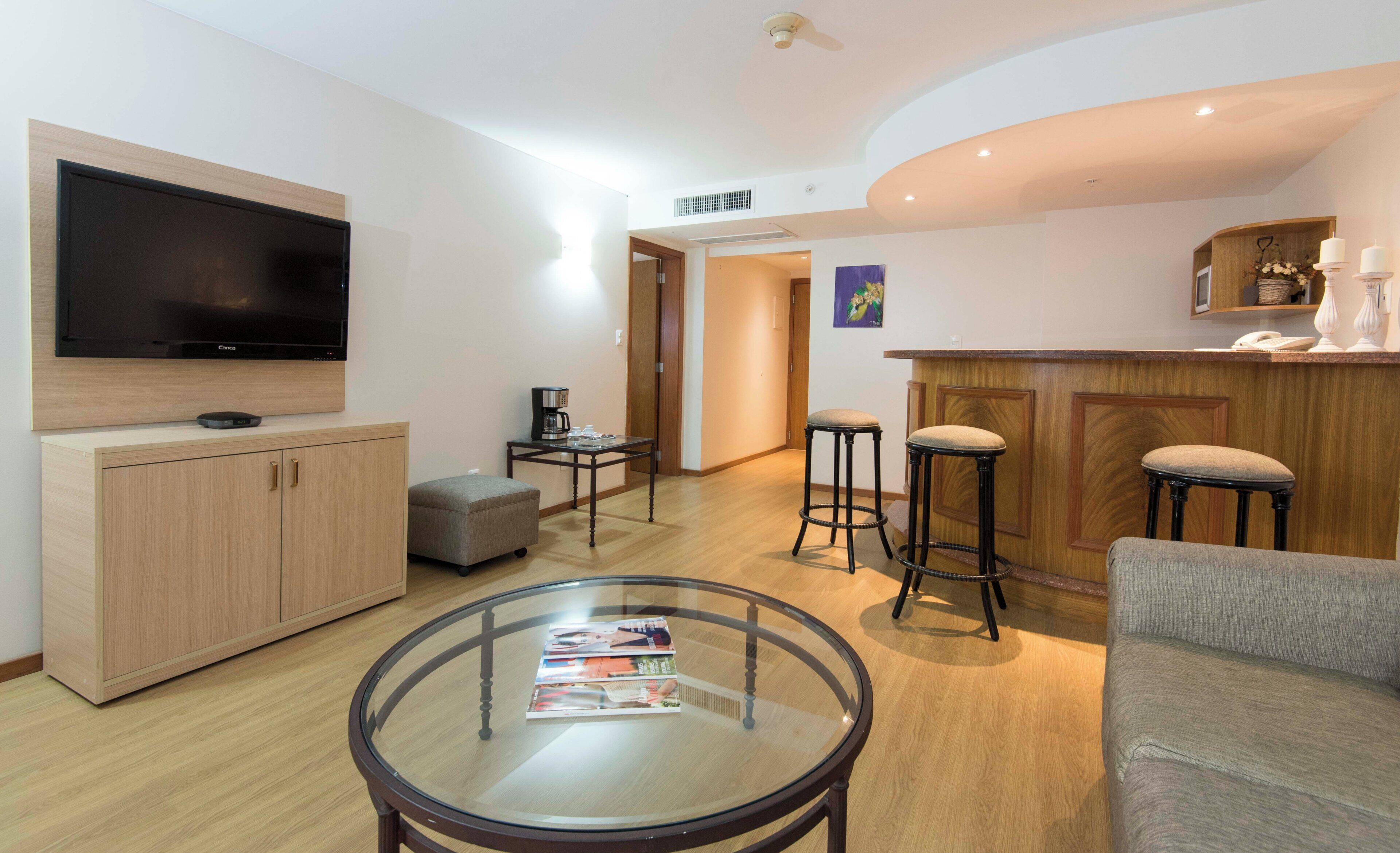 Een moderne woonkamer met een flatscreen televisie, een glazen salontafel, een bank en een bar met krukjes.