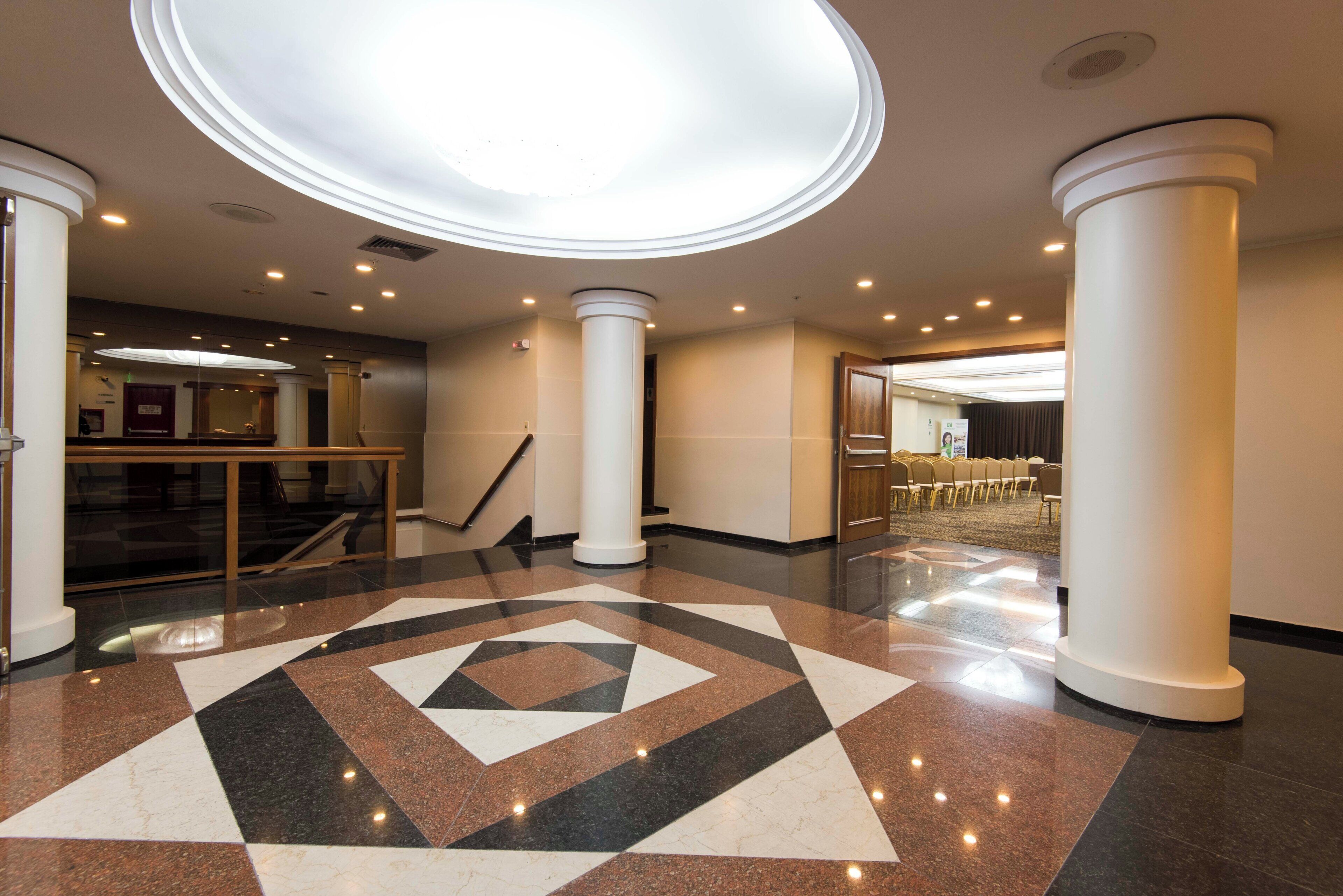 Un vestíbulo de hotel con piso de diseño geométrico, una escalera y un área de descanso con sillas.