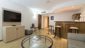 A modern living room with a flat-screen TV, a glass coffee table, a sofa, and a bar area with stools. - Holiday Inn Montevideo by IHG (Montevideo)