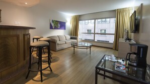 A modern living room with a sofa, two bar stools, a coffee table, and a television. - Holiday Inn Montevideo by IHG (Montevideo)