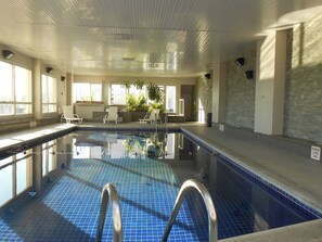 An indoor swimming pool with clear water, a tiled floor, and a metal ladder.