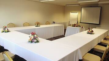 Un salón de conferencias con una larga mesa, sillas y una pantalla de proyector.