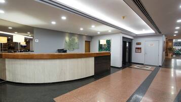 A hotel reception area with a curved reception desk, a wall-mounted information board, and a door leading to another room.